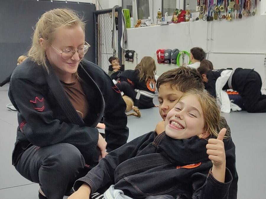 Eine Trainerin und zwei Kinder freuen sich gemeinsam beim BJJ-Training