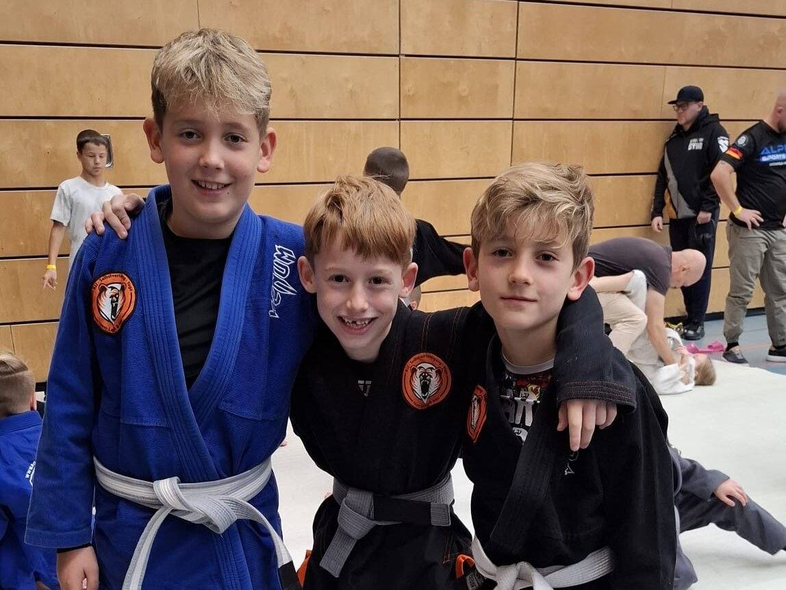 Drei Kinder stehen nach dem BJJ-Training Arm in Arm auf der Matte